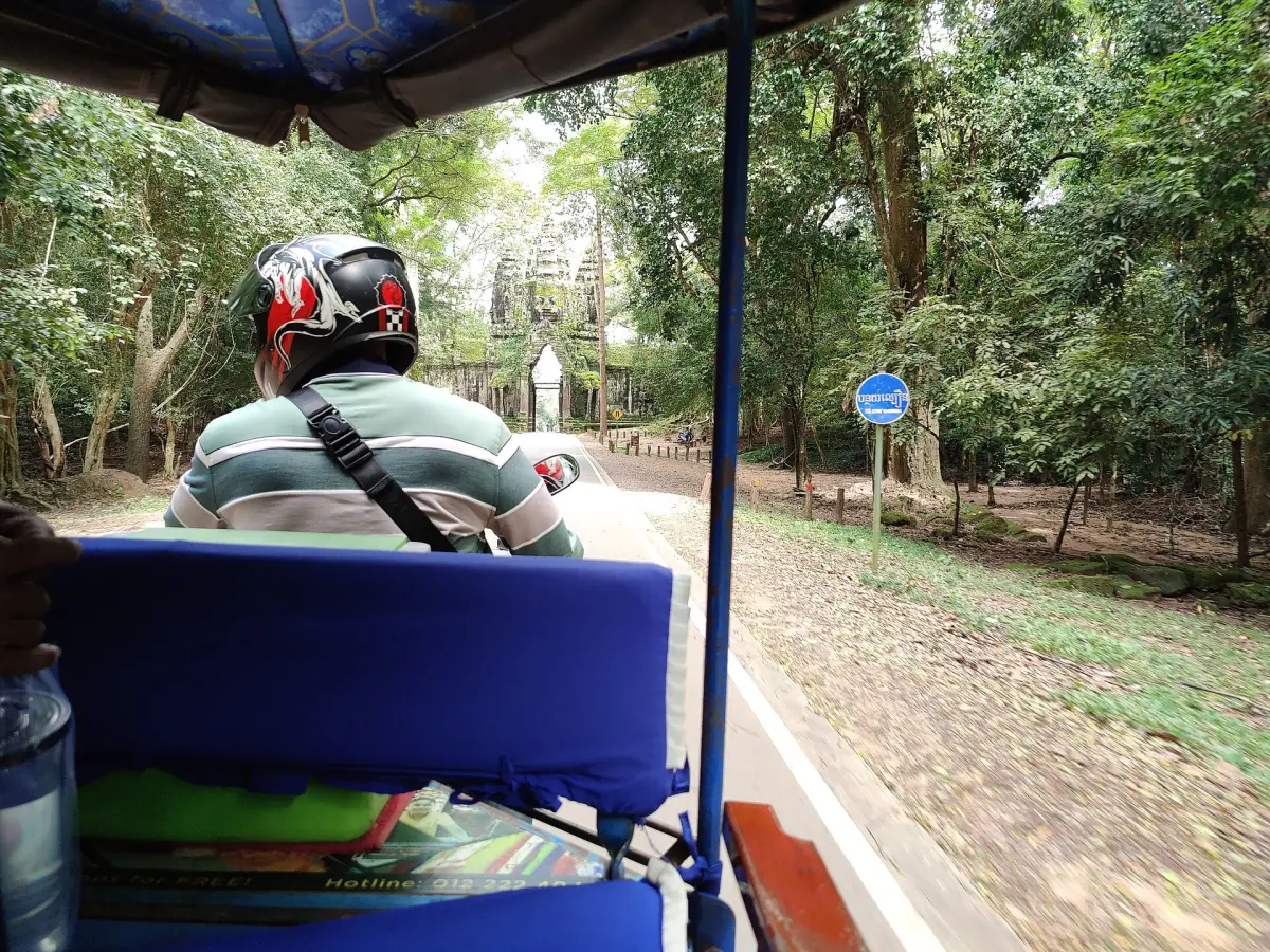 Tuk-tuk driver on a shaded road with a blue seat in front